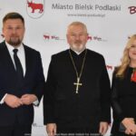 Uśmiechnięci ludzie w trakcie powitania na tle ścianki.