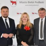 Uśmiechnięci ludzie w trakcie powitania na tle ścianki.