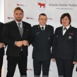 Uśmiechnięci ludzie w trakcie powitania na tle ścianki.