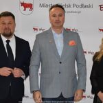 Uśmiechnięci ludzie w trakcie powitania na tle ścianki.