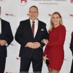 Uśmiechnięci ludzie w trakcie powitania na tle ścianki.