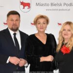 Uśmiechnięci ludzie w trakcie powitania na tle ścianki.