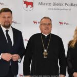 Uśmiechnięci ludzie w trakcie powitania na tle ścianki.