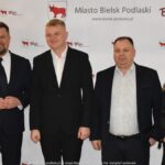 Uśmiechnięci ludzie w trakcie powitania na tle ścianki.