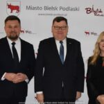 Uśmiechnięci ludzie w trakcie powitania na tle ścianki.