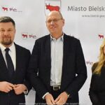 Uśmiechnięci ludzie w trakcie powitania na tle ścianki.