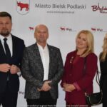 Uśmiechnięci ludzie w trakcie powitania na tle ścianki.