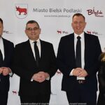 Uśmiechnięci ludzie w trakcie powitania na tle ścianki.