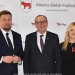 Uśmiechnięci ludzie w trakcie powitania na tle ścianki.