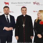 Uśmiechnięci ludzie w trakcie powitania na tle ścianki.