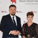 Uśmiechnięci ludzie w trakcie powitania na tle ścianki.