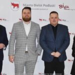 Uśmiechnięci ludzie w trakcie powitania na tle ścianki.