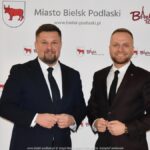 Uśmiechnięci ludzie w trakcie powitania na tle ścianki.