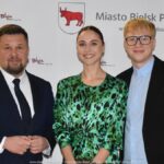 Uśmiechnięci ludzie w trakcie powitania na tle ścianki.