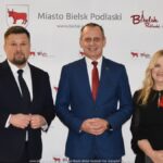 Uśmiechnięci ludzie w trakcie powitania na tle ścianki.