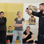 Policjanci i kobiety podczas spotkania. Policjant prezentuje zasady użycia miotacza gazowego.