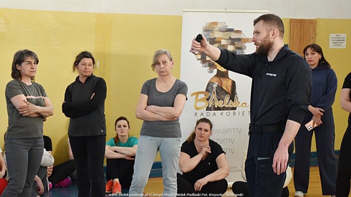 Policjanci i kobiety podczas spotkania. Policjant prezentuje zasady użycia miotacza gazowego.