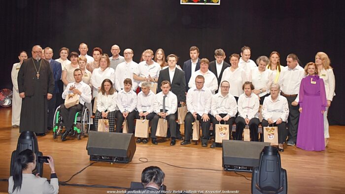 Uroczystości jubileuszowe. Domownicy ŚDS-u stoją w dwóch szeregach na scenie i pozują do grupowego zdjęcia. Towarzyszą im ich opiekunowie.