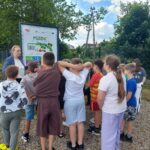 dzieci stoją przed tablicą informacyjną i słuchają wykładu