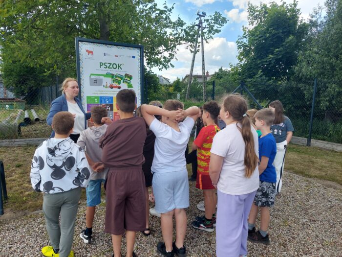dzieci stoją przed tablicą informacyjną i słuchają wykładu