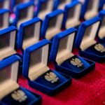 Zdjęcie przypinek w kształcie orła z godła Polski w pudełkach ułożonych na czerwonym stole.