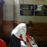 Kobieta składa wiązankę pod pamiątkową tablicą w kościele.