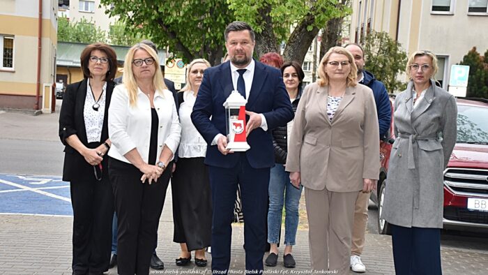 Grupa pracowników urzędu podczas uroczystości. Kilka osób pozuje do zdjęcia. Na pierwszym planie mężczyzna w garniturze trzyma biało-czerwony znicz z herbem miasta Bielsk Podlaski.