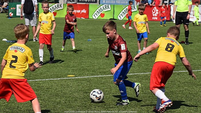 Zawody dzieci na stadionie. Chłopcy grający w piłkę na zielonym boisku. W tle reklamy organizatorów i sponsorów.