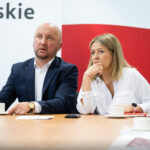 Samorządowcy i uczestnicy spotkania siedzący za stołem.