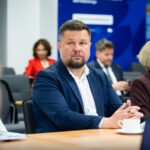 Samorządowcy i uczestnicy spotkania siedzący za stołem.