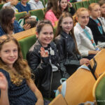 Uroczyste zakończenie roku akademickiego. Studentki siedzą w ławie i pozują do zdjęcia.