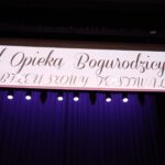 Napis nad sceną: Pod Opieką Bogurodzicy".