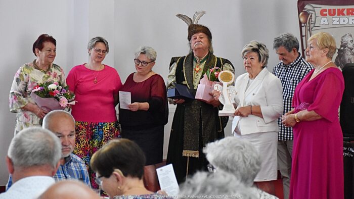 Wręczenie nagród. Dwaj mężczyźni i pięć kobiet stoją prze zgromadzonymi i wręczają sobie statuetki. Przed nimi siedzą uczestnicy spotkania.