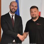 Dwaj mężczyźni pozują do zdjęcia ściskając sobie dłonie w geście przyjaźni i porozumienia.
