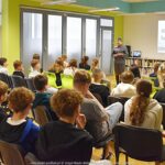 Młodzież siedząca na krzesłach podczas wykładu w bibliotece.