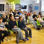 Młodzież siedząca na krzesłach podczas wykładu w bibliotece.