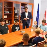 Wnętrze gabinetu. Mężczyzna stoi i mówi do siedzących wokół stołu młodych chłopców.
