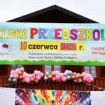 Szyld z nazwą imprezy, wiszący na tle drewnianego budynku.