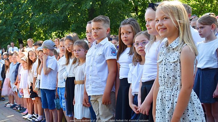 Dzieci podczas zakończenia roku szkolnego. Dzieci stoją na trybunach amfiteatru podczas hymnu państwowego.