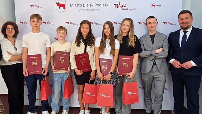 Wspólne zdjęcie młodych radnych, burmistrza i urzędniczek na tle ścianki reklamowej miasta.