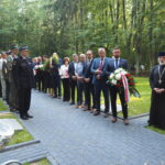stojących w rzędzie, pierwszy trzyma biało niebieski wieniec