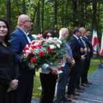 stojących w rzędzie, pierwszy trzyma biało niebieski wieniec