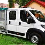 Zdjęcie samochodu dostawczego na parkingu, wśród zieleni.