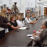 Kilkanaście osób dorosłych siedzi za stołem podczas spotkania informacyjnego.