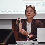 Kobieta prowadzi prezentację dla kilkunastu osób w sali konferencyjnej.