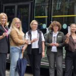 Siedem kobiet stoi przed autokarem na tle bramy Białowieskiego Parku Narodowego.