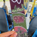 Kolorowy bilet trzymany w kobiecej dłoni na tle wnętrza autobusu.